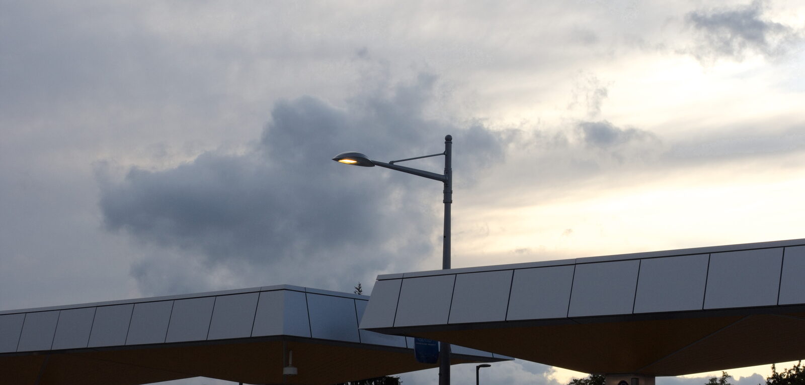 Street lamp and dark clouds above two angular canopy roofs