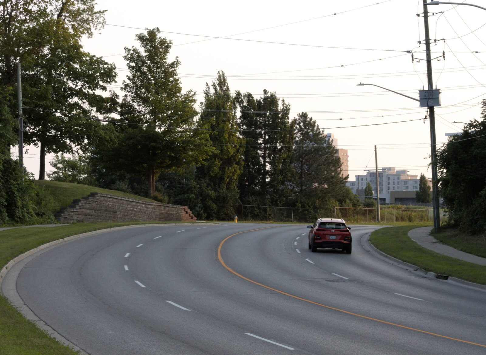 Curved road with a red car, trees and power lines under an overcast sky